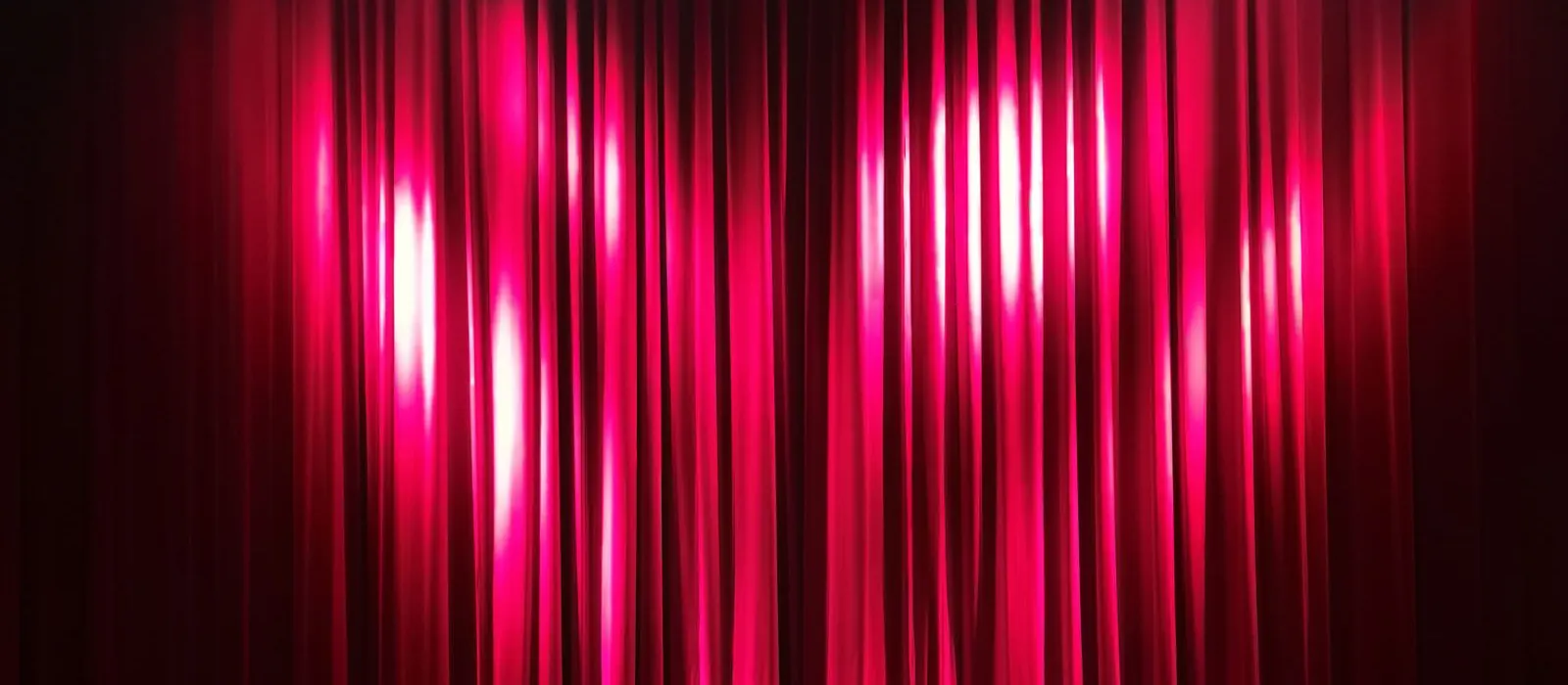 Sala teatrale con il sipario rosso illuminato e le poltrone vuote