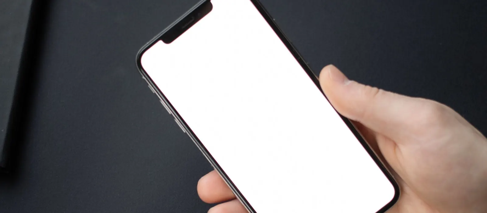 Mani che tengono uno smartphone con lo schermo vuoto su una scrivania scura